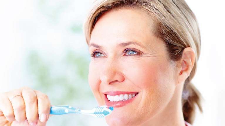 A woman smiling while brushing her teeth