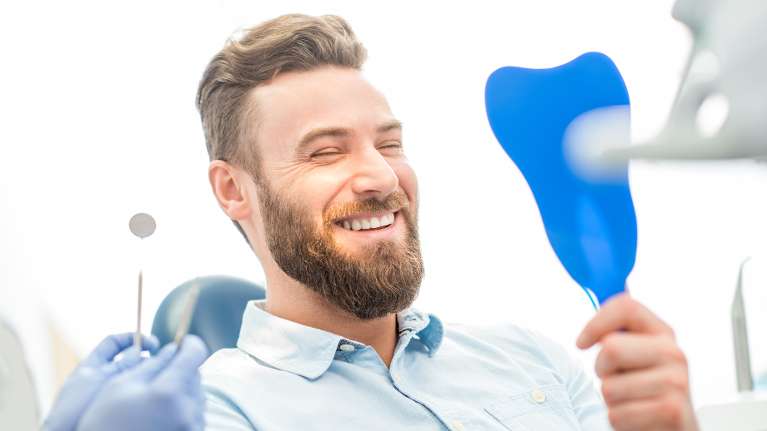 Patient looking into hand mirror after dental crown procedure in Brandon, FL