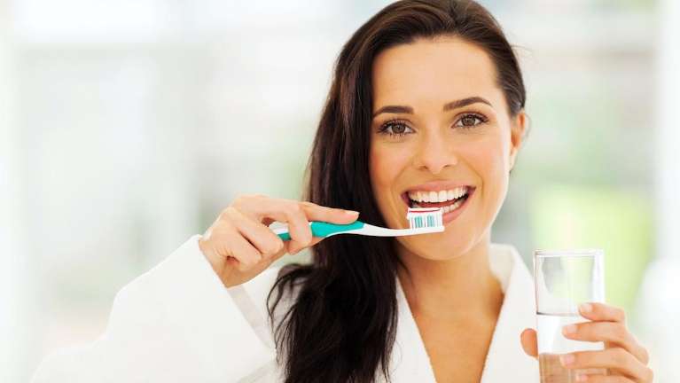 A woman brushing her teeth | maintaining oral health
