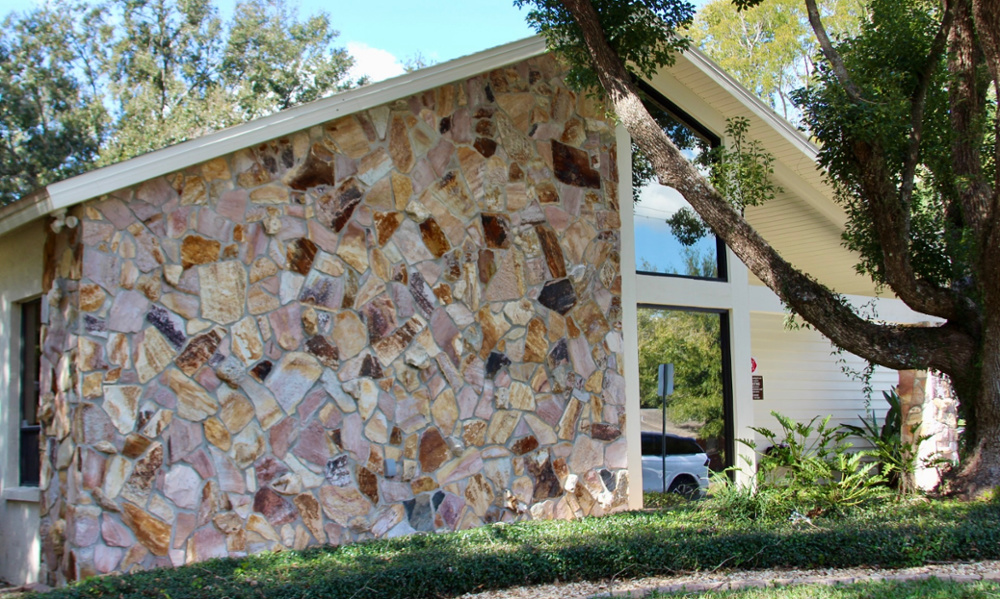 Exterior of McAuley Dental office featuring a stone facade, large windows, and mature trees surrounding the building.